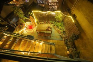 A rooftop garden with a wooden deck, seating area, and string lights.