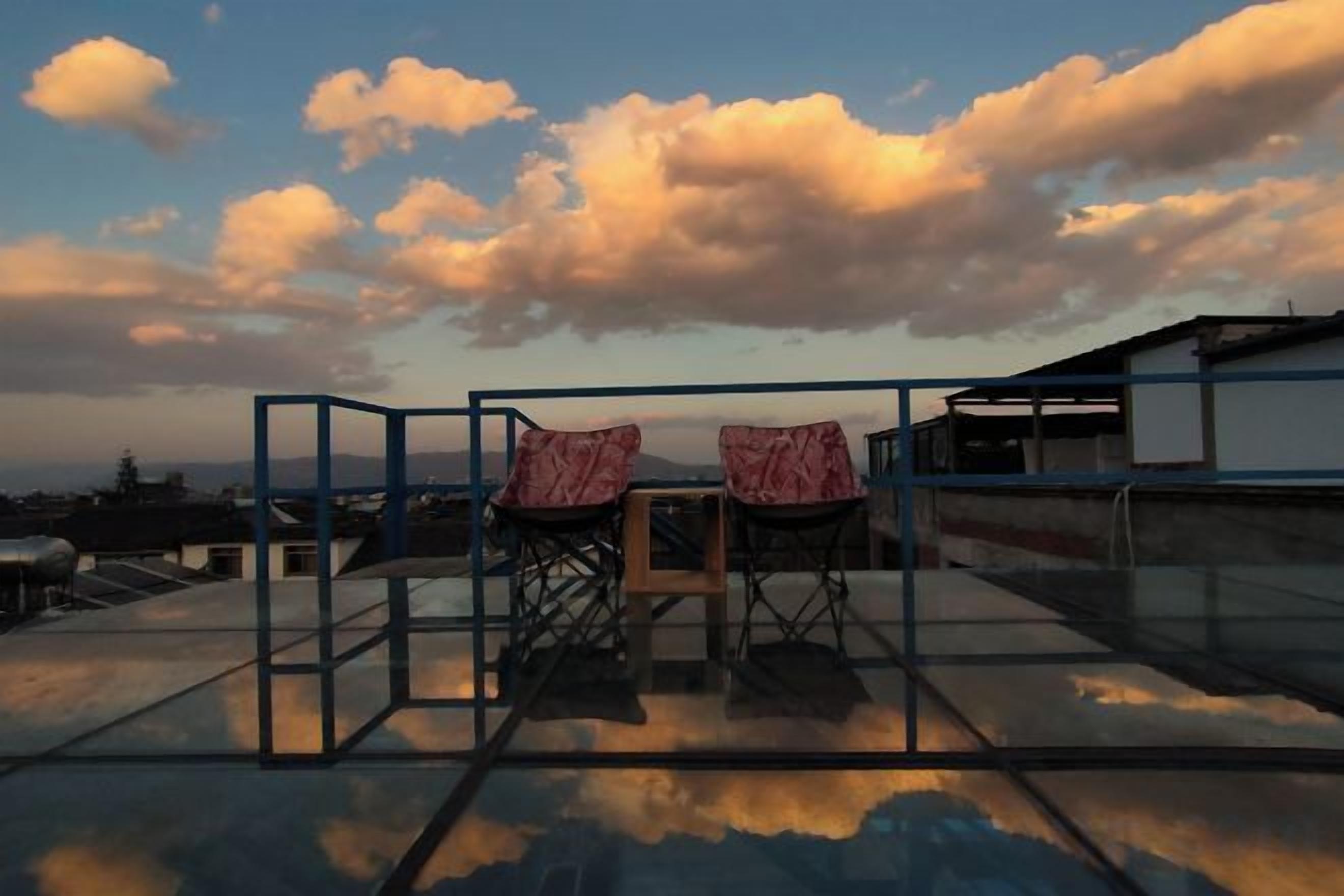 Terraza en la azotea con dos sillas y una mesa, con vistas a un paisaje urbano con edificios y cielo despejado.