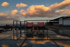Terraza en la azotea con dos sillas y una mesa, con vistas a un paisaje urbano con edificios y cielo despejado.