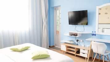 Et hotelværelse med seng, fjernsyn hængt på væggen, et skrivebord med stol og et vindue med gardiner.