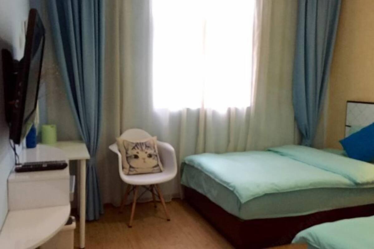 A bedroom with a bed, a chair, a desk, and a window with curtains.