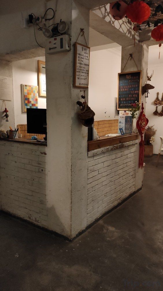 Zona de recepción con mostrador de ladrillo, una pizarra con texto y diversas decoraciones, incluyendo un peluche y un adorno rojo colgante.