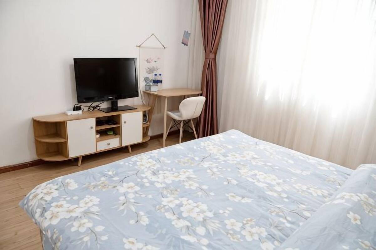 A bedroom with a bed, a TV, a desk, and a chair.