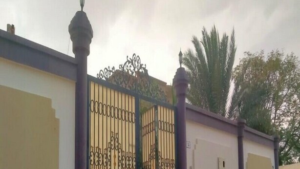 A gated entrance with ornate metalwork, a white wall, and a small utility box. - Al Dhait Residence (Ras Al Khaimah)