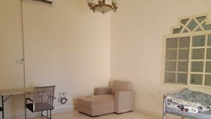A room with a ceiling fan, an air conditioner, a chandelier, a bed, a desk, and a chair. - Al Dhait Residence (Ras Al Khaimah)