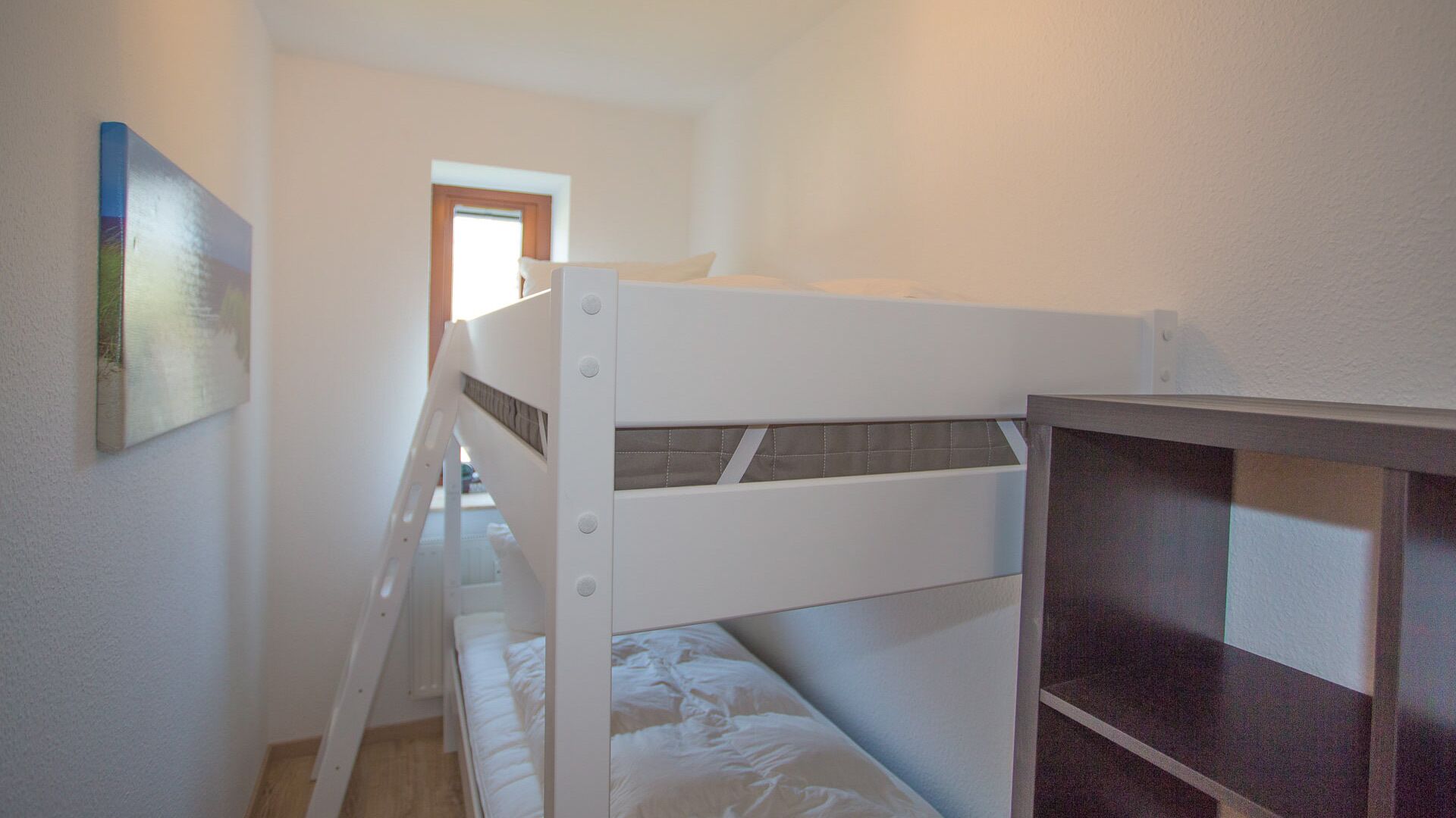 Habitación con literas, ventana, puerta y un cuadro en la pared.