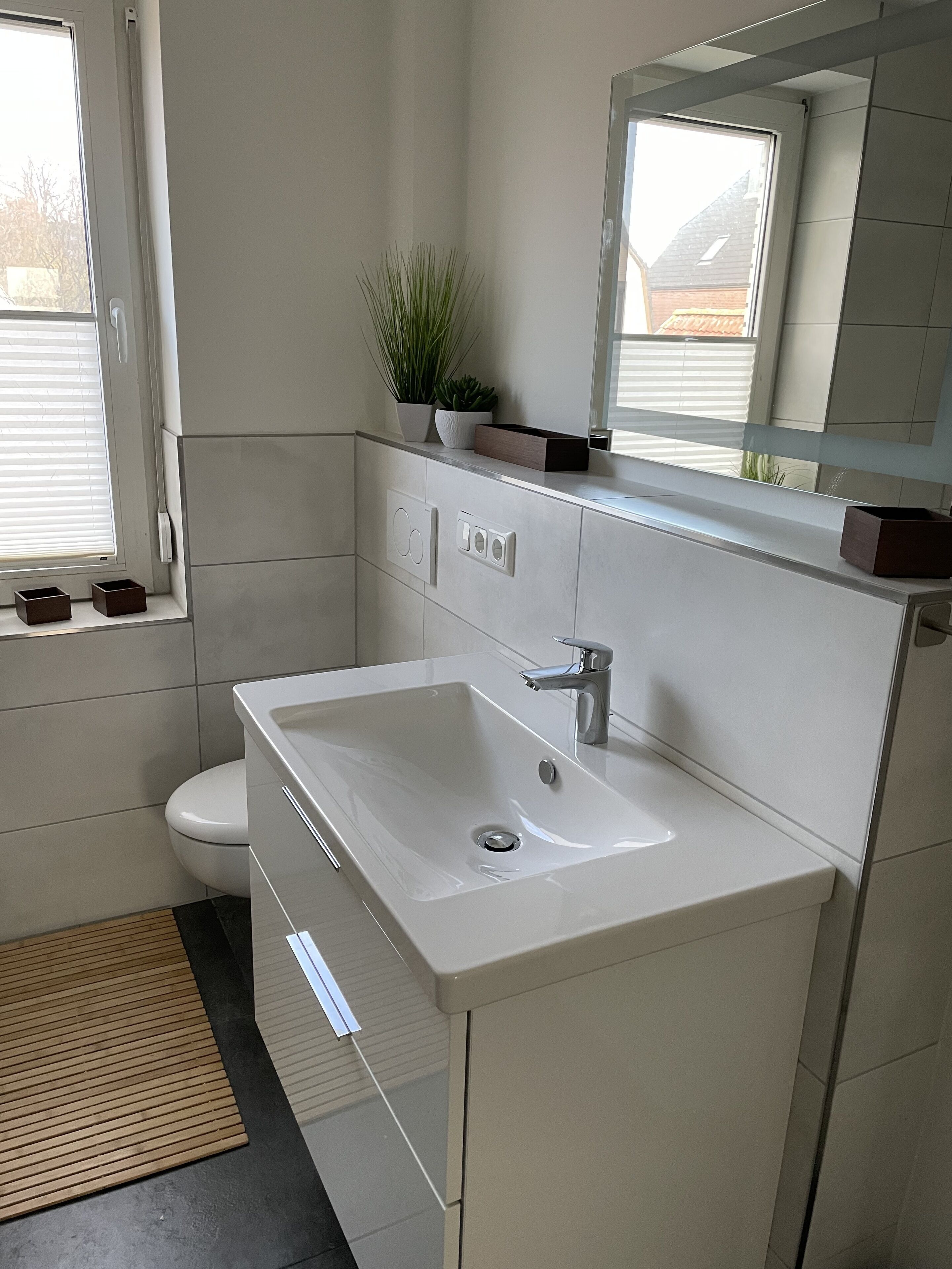 Un baño moderno con un lavabo blanco, un inodoro y una ventana con persianas.