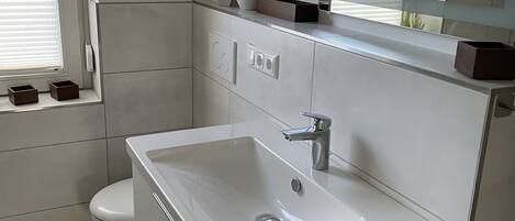 Un baño moderno con un lavabo blanco, un inodoro y una ventana con persianas.