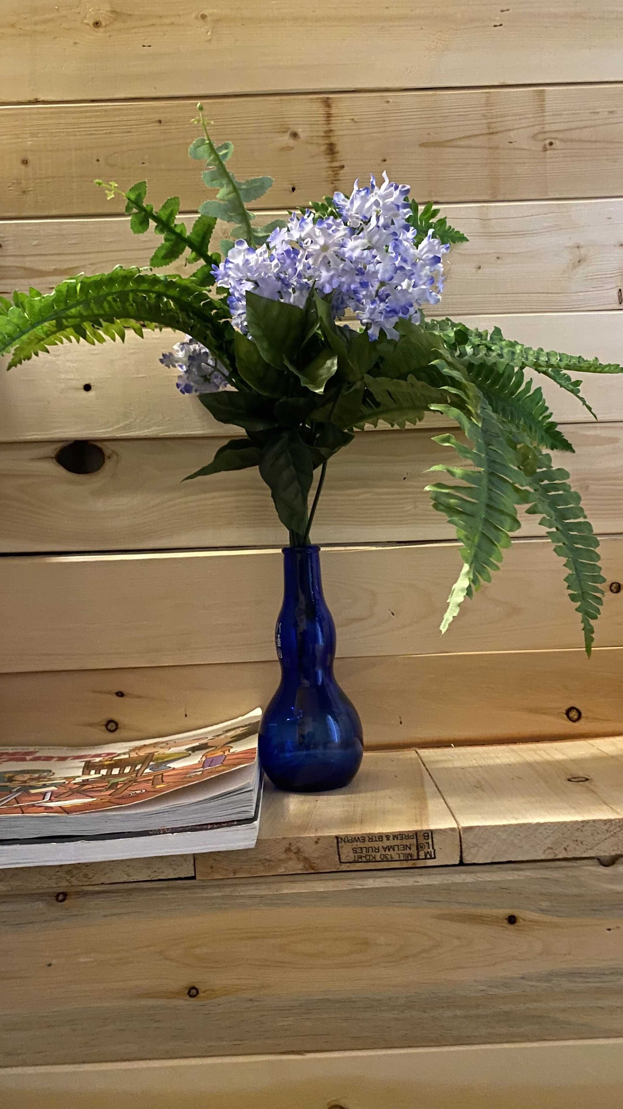 Um vaso azul com flores e folhas verdes sobre uma superfície de madeira.