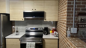 Una cocina con horno de acero inoxidable, cafetera y pared de ladrillo.