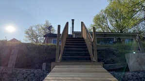 Una scala in legno conduce a una casa con un garage, circondata da alberi e un cielo sereno.