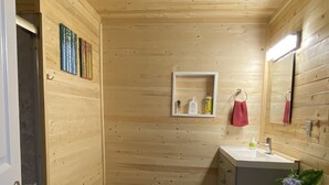 A wooden-paneled bathroom with a toilet, sink, and mirror. There are wooden floors and a small shelf with toiletries. - Tranquility on the River (Britt)