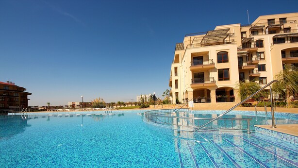 A swimming pool with clear blue tiles, surrounded by a building with balconies and a tiled deck. - Sorrento - Menada Apartments (Sveti Vlas)