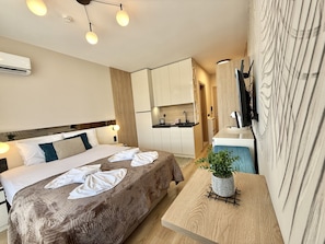 A compact hotel room with a bed, bedside table, and a small kitchenette.
