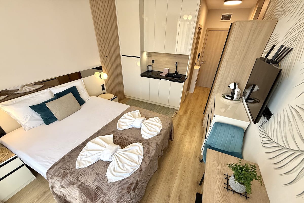 A compact hotel room with a bed, a small desk, a kitchenette, and a bathroom.