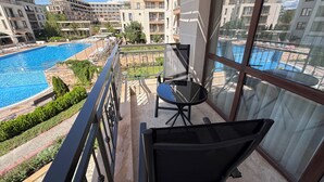 A balcony with a glass door, a chair, and a view of a swimming pool and buildings. - Sorrento - Menada Apartments (Sveti Vlas)