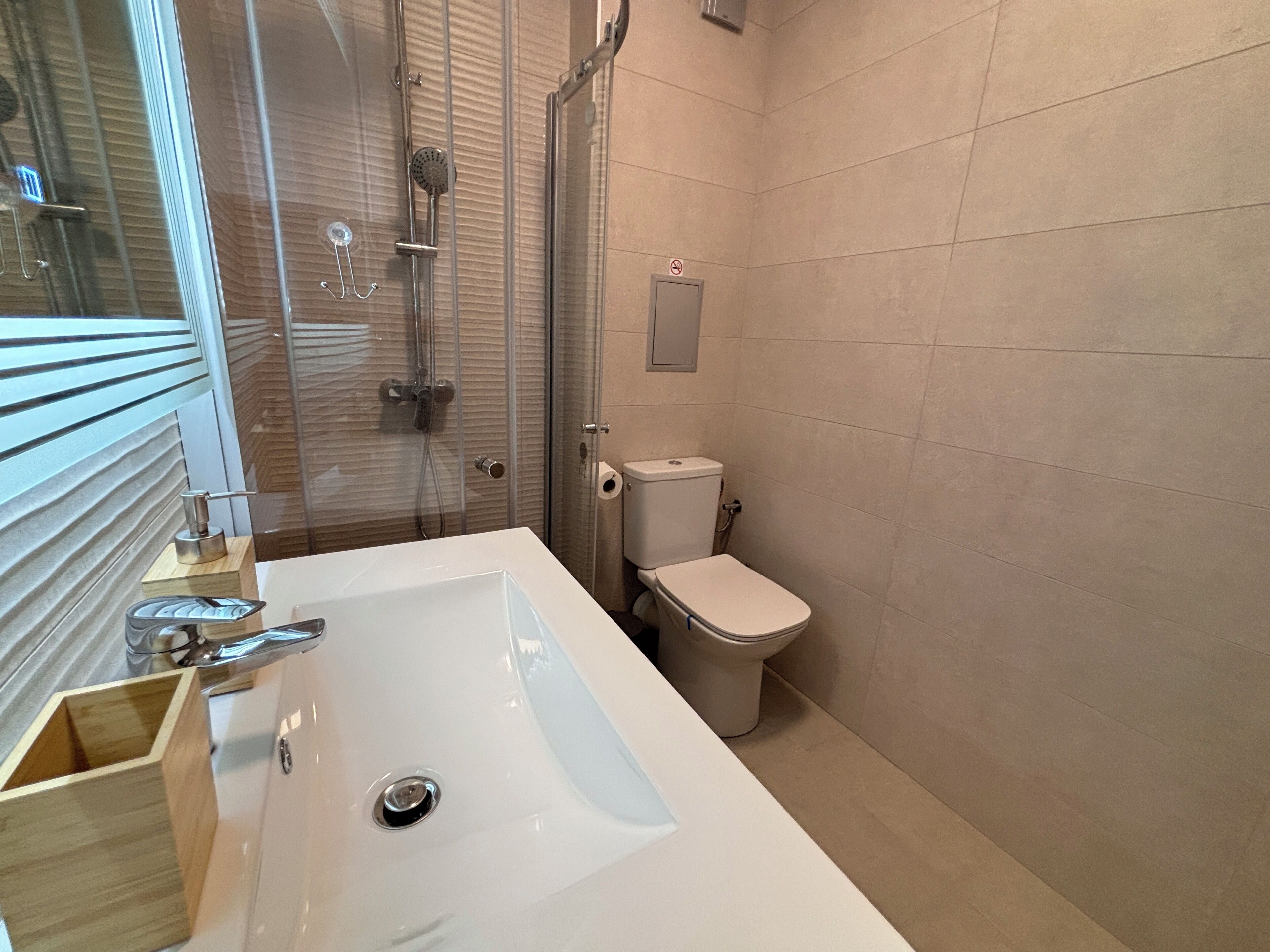 Un baño moderno con un lavamanos grande de color blanco, una ducha con cerramiento de vidrio y un inodoro.