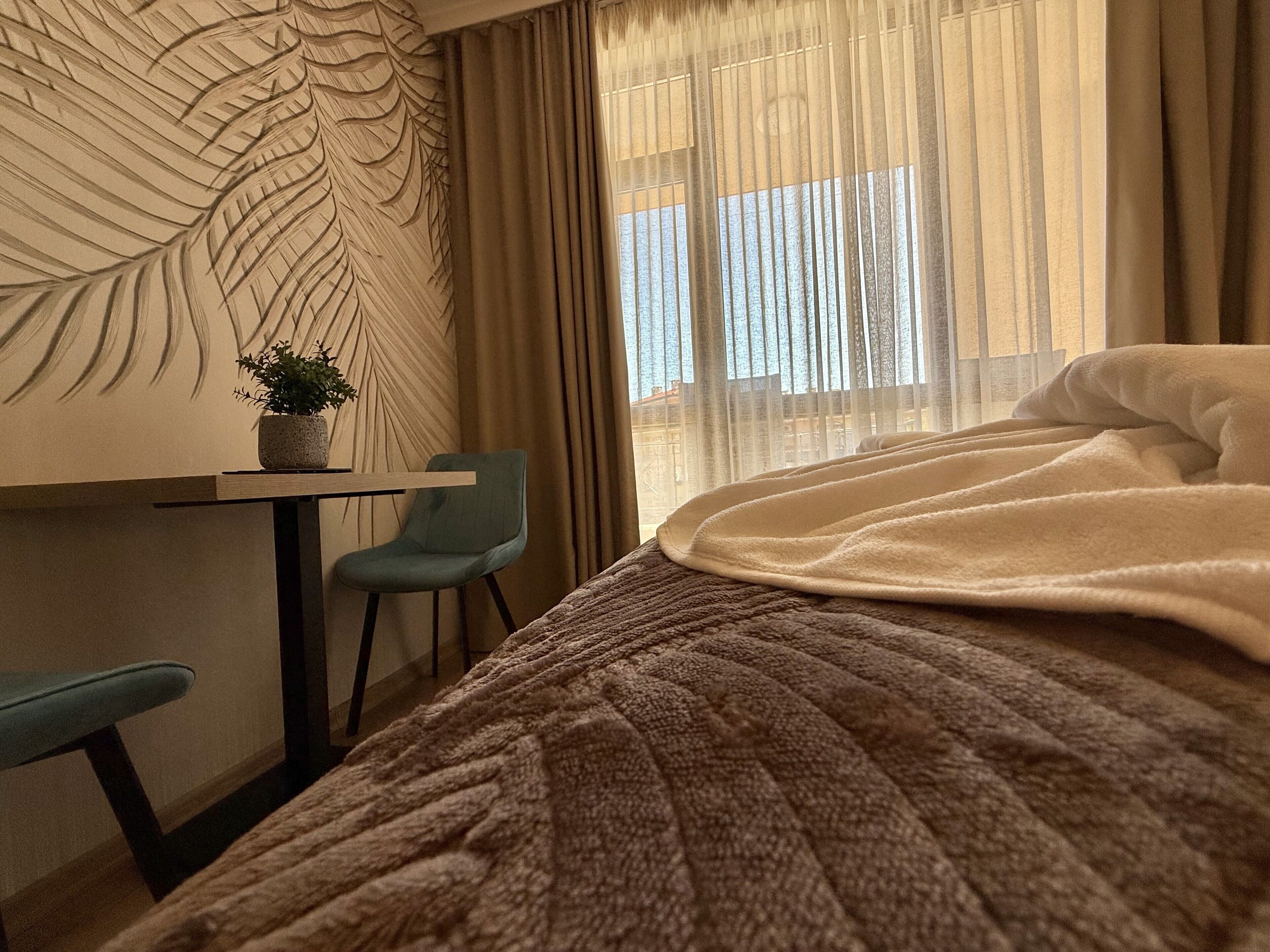 A hotel room with a bed, a desk, a chair, and a large window with curtains.
