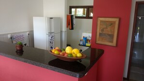 Eine Küche mit Obstschale auf der Arbeitsfläche, einem Kühlschrank und einem Fenster mit Blick auf Grünflächen.