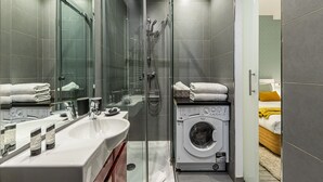 Een moderne badkamer met een glazen douchecabine, een wastafel met spiegel en een wasmachine.