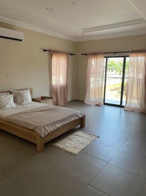 A bedroom with a large bed, a nightstand, and a window with sheer curtains.