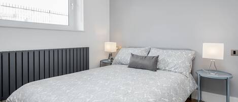A bedroom with a bed, two bedside tables, a window, and a radiator.