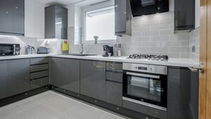 A modern kitchen with grey cabinets, a built-in oven, a microwave, and a coffee maker. - Luxury Chic Apartment near Canary Wharf, Excel, O2 & Stratford (London)