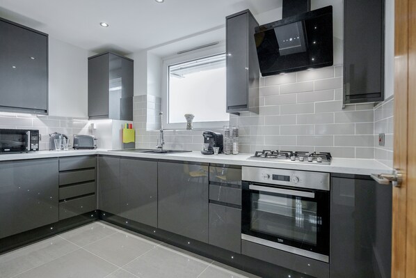 A modern kitchen with grey cabinets, a built-in oven, a microwave, and a coffee maker. - Luxury Chic Apartment near Canary Wharf, Excel, O2 & Stratford (London)