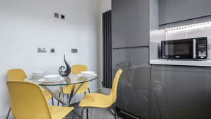 A modern kitchen with a built-in microwave, a glass dining table with yellow chairs, and a black refrigerator. - Luxury Chic Apartment near Canary Wharf, Excel, O2 & Stratford (London)