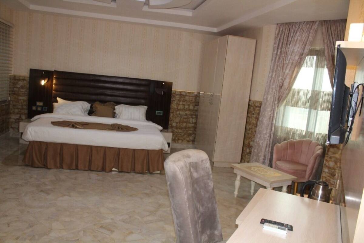 Een hotelkamer met een groot bed, een kleine tafel, een stoel, een televisie en een raam met gordijnen.