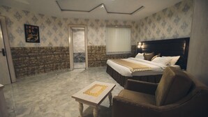 A hotel room with a bed, a sofa, a small table, a door, and a window with blinds. - Candellux Imperial Hotel and Suites (Abuja)