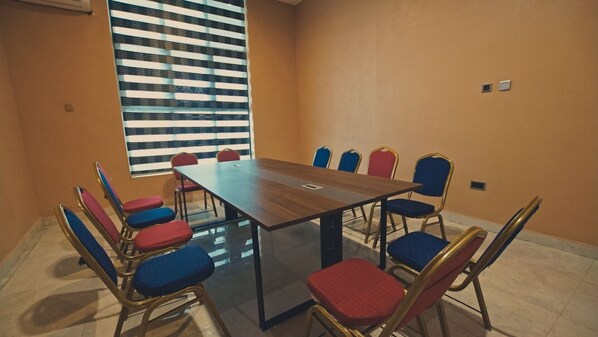 Una sala de conferencias con una larga mesa y sillas, una ventana con persianas y una pared lisa.