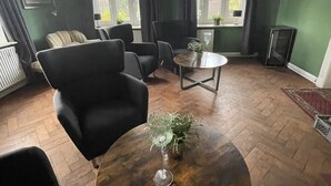 Une pièce comprenant une table ronde en bois, deux fauteuils, une petite table d’appoint avec une plante et un lustre.