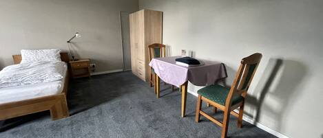 A bedroom with a bed, a desk with a chair, a wardrobe, and a carpeted floor.