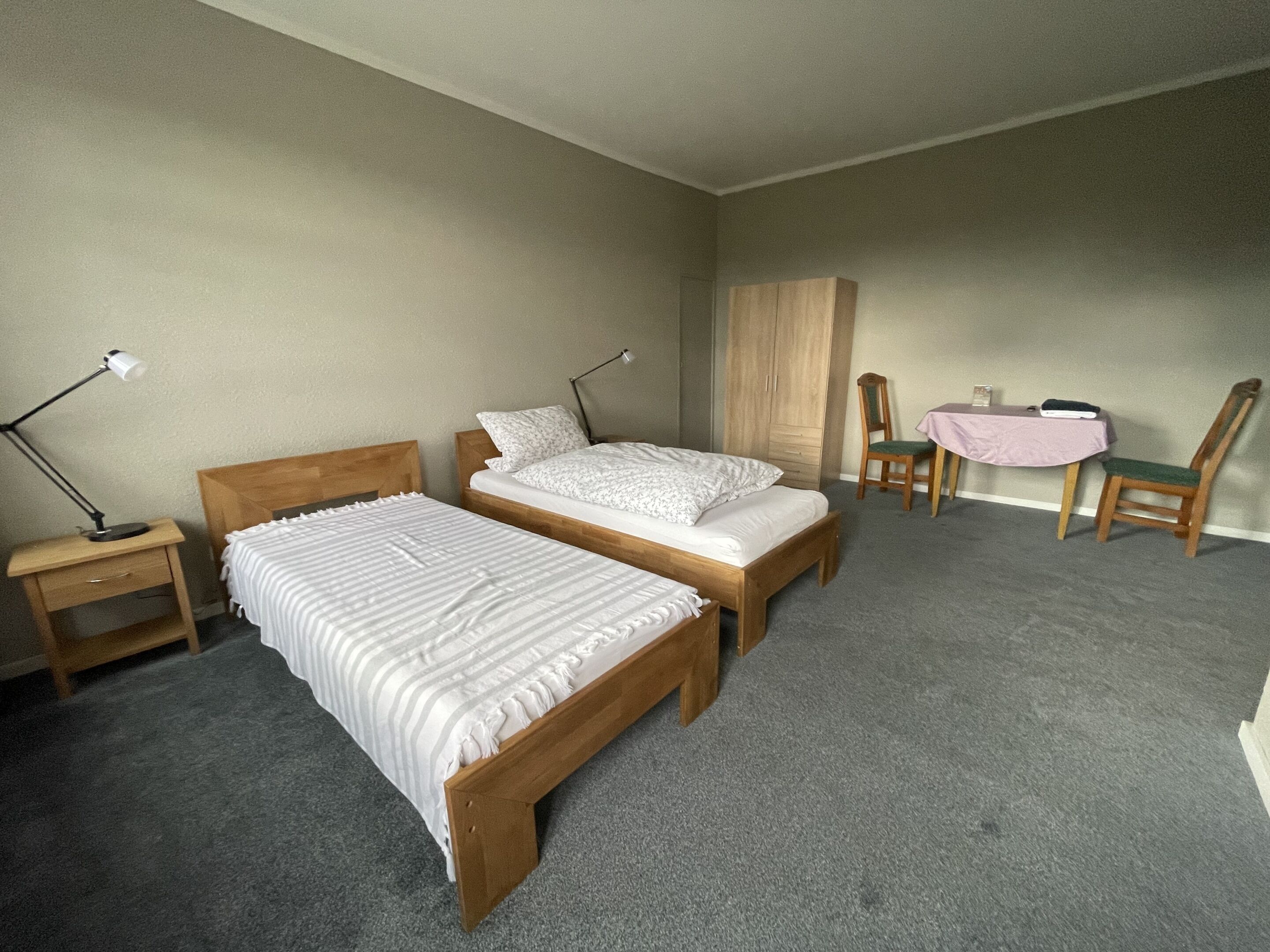 A bedroom with two beds, a nightstand, a desk, a chair, and a wardrobe.
