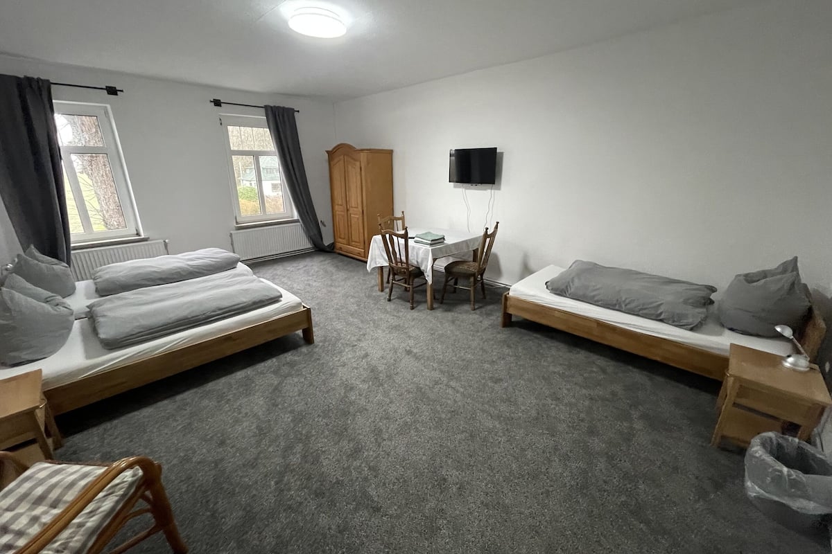 A room with two single beds, a small table with chairs, a TV mounted on the wall, and a radiator.