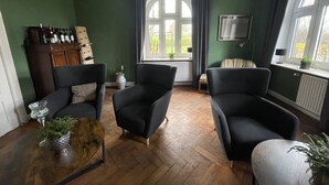 Un salon aux murs vert foncé, doté d’un parquet et de meubles modernes, notamment deux fauteuils noirs et une table basse en bois sur laquelle est posée une plante.