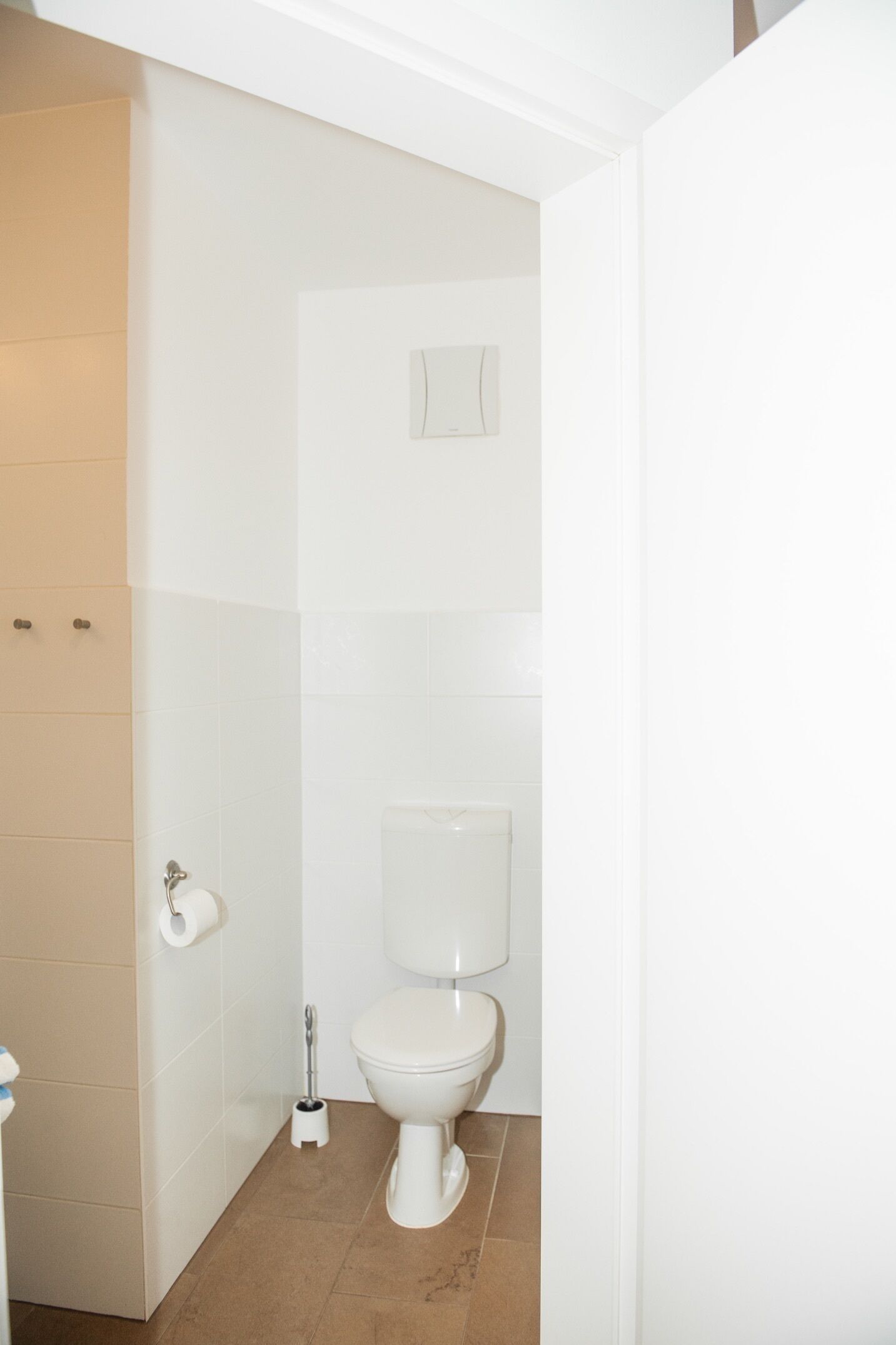 Un baño con un inodoro, un rollo de papel higiénico y un cepillo para el inodoro.