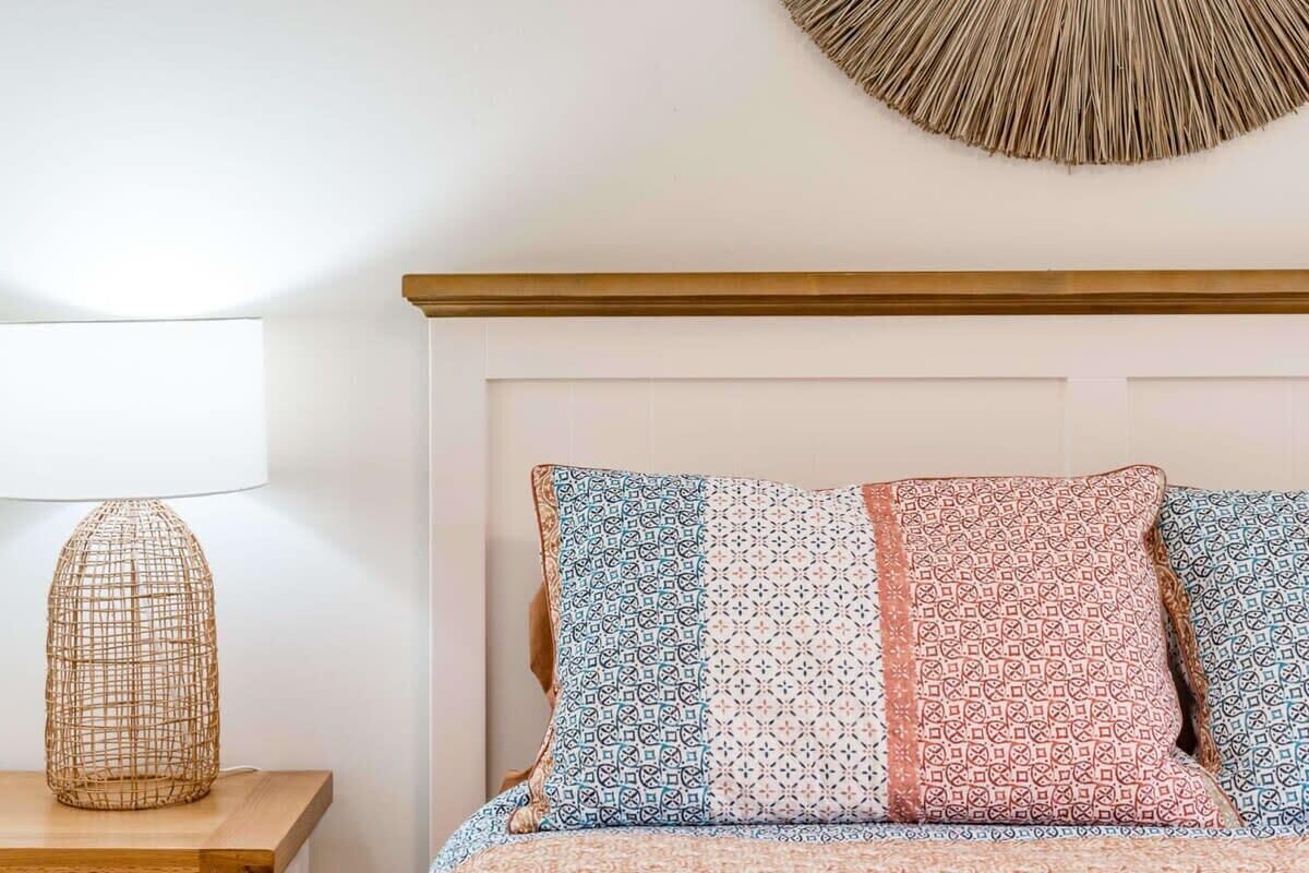 Una cama con almohadones estampados, una lámpara tejida y un adorno circular en la pared.