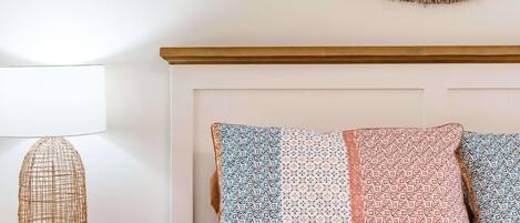 Una cama con almohadones estampados, una lámpara tejida y un adorno circular en la pared.