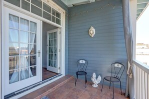 A porch with two chairs, a decorative wall piece, and a sliding glass door leading to a patio. - The Retreat on Broad @ Trustees' Garden (Savannah)