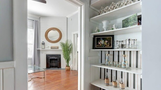 A room with a fireplace, a mirror, and a bookshelf with decorative items. - The Retreat on Broad @ Trustees' Garden (Savannah)