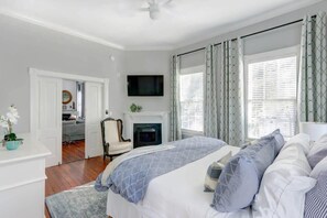 A bedroom with a bed, a TV, a fireplace, and a view of the outside. - The Retreat on Broad @ Trustees' Garden (Savannah)
