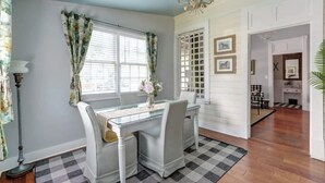 A dining area with a glass table, white chairs, and a checkered rug. - The Cottage @ Trustees' Garden | Walk To River! (Savannah)