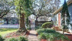 A pathway leading to a house with a red door, surrounded by lush greenery and a white picket fence. - The Cottage @ Trustees' Garden | Walk To River! (Savannah)