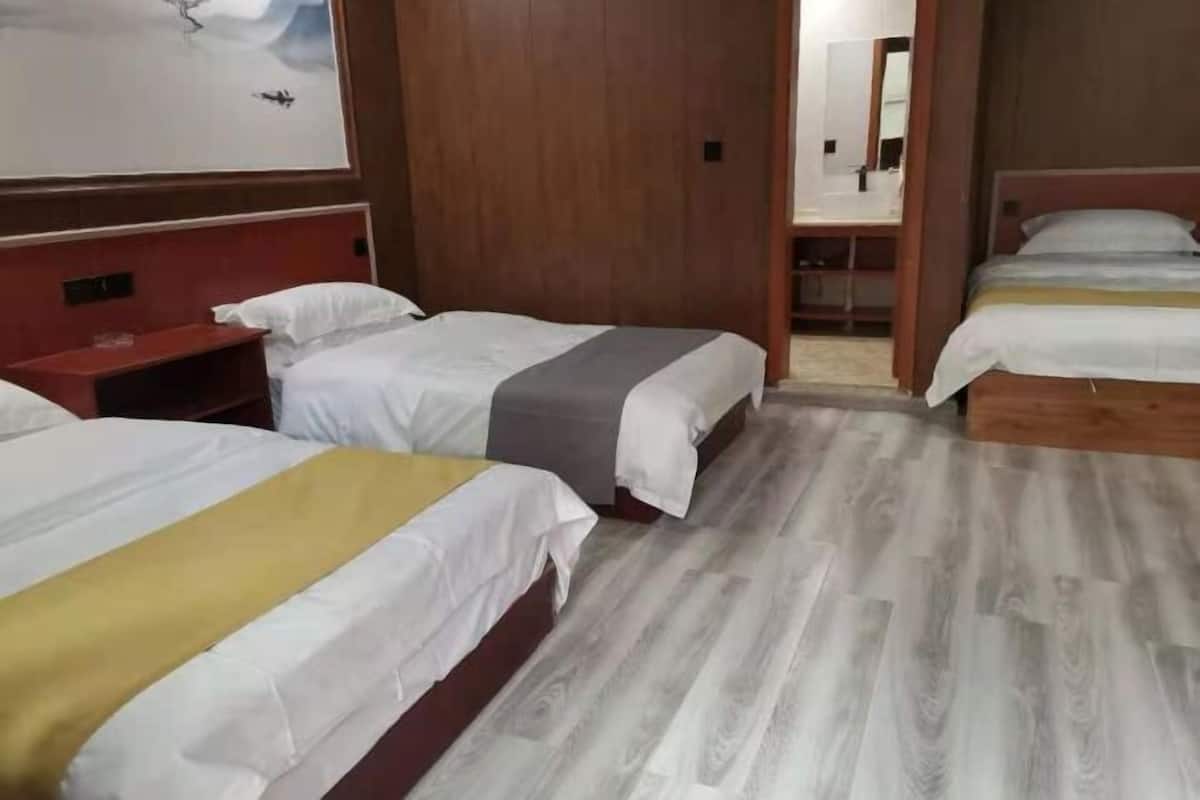 Ein Hotelzimmer mit drei Betten, Holzboden und einem großen Spiegel.