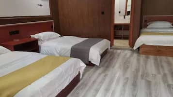 Habitación de hotel con tres camas, suelo de madera y un espejo grande.