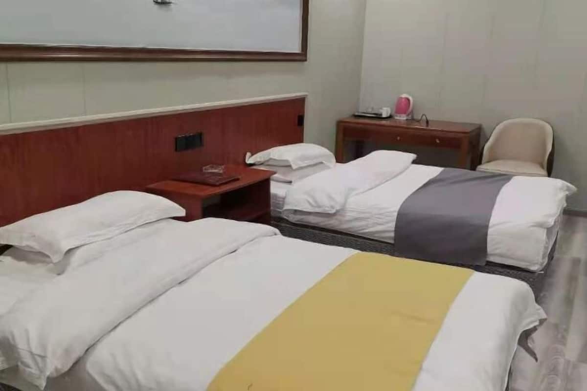 Ein Hotelzimmer mit zwei Betten, einem Holzkopfende, einem Nachttisch mit Lampe, einem Sessel und einem kleinen Tisch mit Telefon und Tasse.