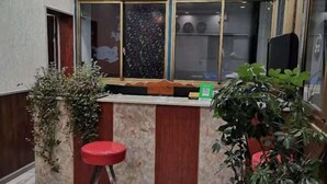 A small reception area with a wooden counter, a red stool, and potted plants. - Gaji Hotel (Gyantse)