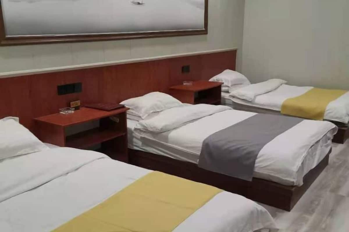 Ein Hotelzimmer mit drei Betten, einem hölzernen Kopfteil, einem großen Spiegel und einem kleinen Tisch mit einem Glas.